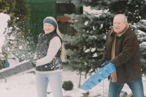 an older woman and man smile as they shovel snow into the air